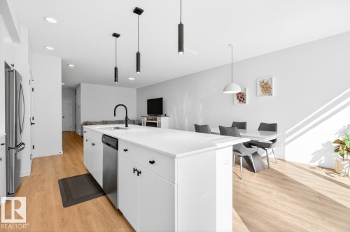 Modern kitchen island with a white countertop and integrated sink, stainless steel dishwasher, and matte black faucet - 17347 100 Street, Edmonton, AB - Indoor Photo Showing Kitchen With Upgraded Kitchen