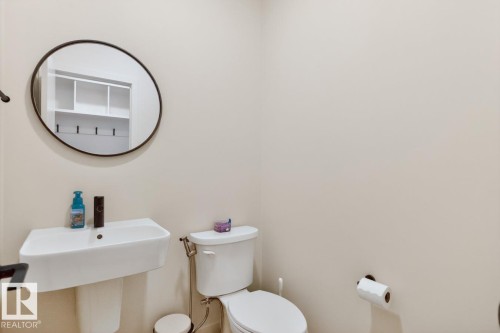 Pedestal sink with white basin, round black-framed mirror, and recessed toilet - 17347 100 Street, Edmonton, AB - Indoor Photo Showing Bathroom