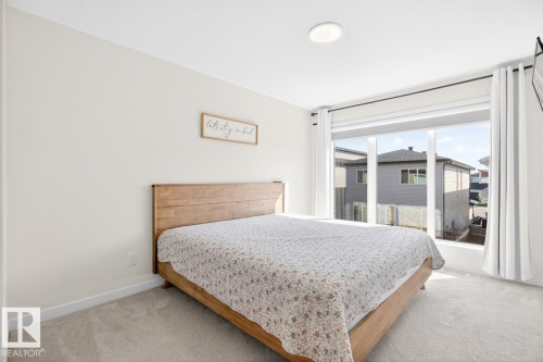 Bedroom featuring light-toned carpeting and a large window with white curtain panels - 17347 100 Street, Edmonton, AB - Indoor Photo Showing Bedroom