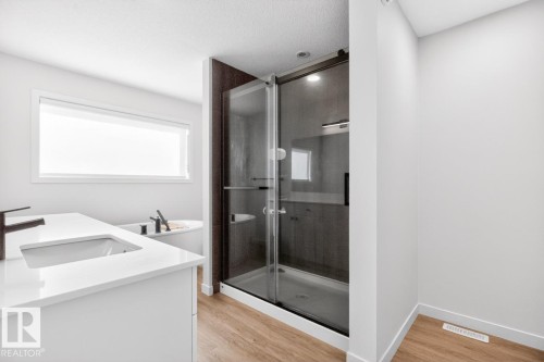 Modern bathroom featuring a glass-enclosed shower, freestanding soaking tub, and a vanity with an integrated sink and dark bronze faucet - 17347 100 Street, Edmonton, AB - Indoor