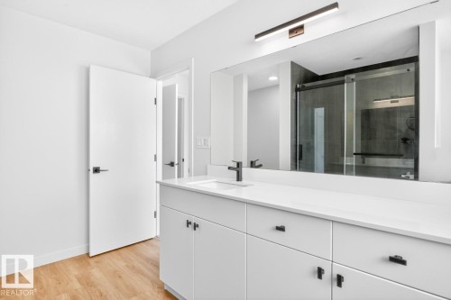 Modern bathroom featuring an expansive white vanity with integrated sink, black hardware, and a large wall-mounted mirror - 17347 100 Street, Edmonton, AB - Indoor Photo Showing Bathroom