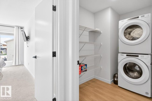 Dedicated laundry area featuring a stacked washer and dryer, wood-finish flooring, and wire shelving - 17347 100 Street, Edmonton, AB - Indoor Photo Showing Laundry Room