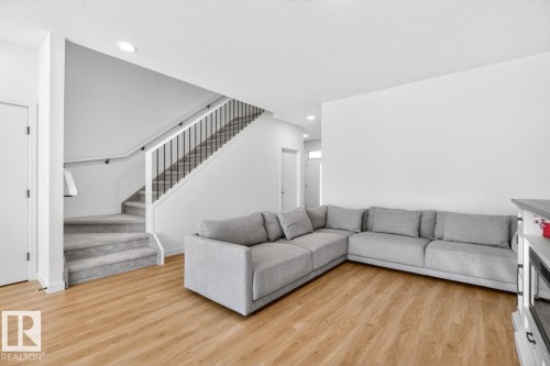 Open-concept living area featuring wood-finish flooring and a carpeted staircase with dark metal balusters - 17347 100 Street, Edmonton, AB - Indoor Photo Showing Living Room