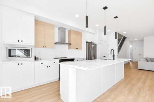 Modern kitchen featuring a large central island, white cabinetry, light wood-finish upper cabinets, stainless steel appliances, and wood-finish flooring - 17347 100 Street, Edmonton, AB - Indoor Photo Showing Kitchen With Upgraded Kitchen