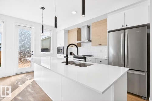 Kitchen featuring a spacious island with a double sink, stainless steel appliances, wood-finish flooring, white cabinetry, and pendant lighting - 17347 100 Street, Edmonton, AB - Indoor Photo Showing Kitchen With Double Sink With Upgraded Kitchen