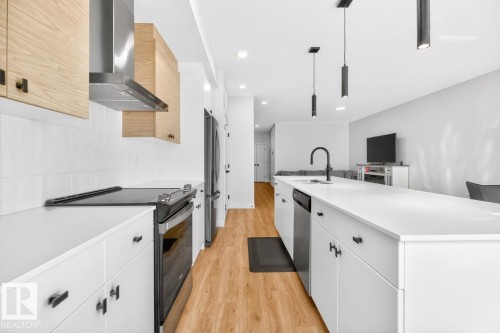 Modern kitchen featuring white cabinetry, light wood-finish upper cabinets, stainless steel appliances, a white tile backsplash, and wood-finish flooring - 17347 100 Street, Edmonton, AB - Indoor Photo Showing Kitchen With Upgraded Kitchen