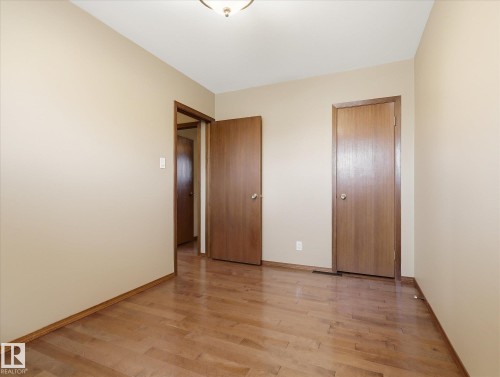 Room featuring wood-finish flooring, neutral wall tones, and multiple wood-panel doors - 13504 116 St Nw, Edmonton, AB - Indoor Photo Showing Other Room