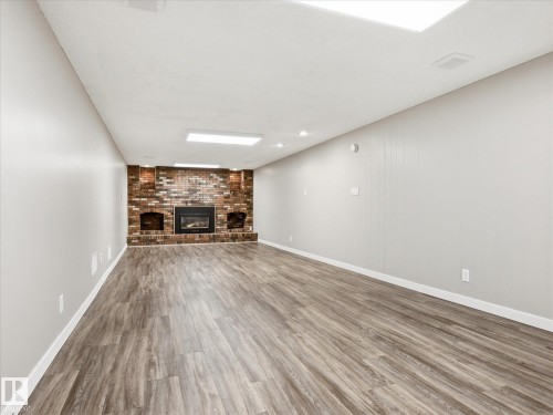 Spacious room featuring wood-finish flooring, a brick fireplace with built-in shelving, recessed lighting, and modern ceiling light fixtures - 13504 116 St Nw, Edmonton, AB - Indoor With Fireplace