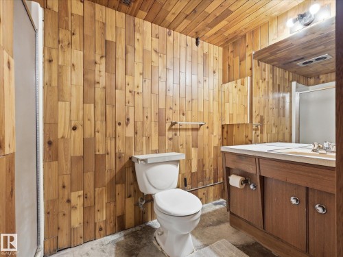 Bathroom featuring extensive wood paneling, a single vanity with wood-finish cabinetry, a white countertop, and a built-in sink - 13504 116 St Nw, Edmonton, AB - Indoor Photo Showing Bathroom