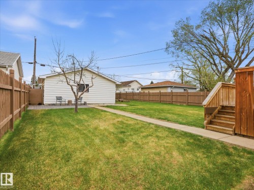 Expansive backyard featuring a large lawn, full perimeter wood fencing, concrete pathway, rear patio, and exterior wooden steps - 13504 116 St Nw, Edmonton, AB - Outdoor