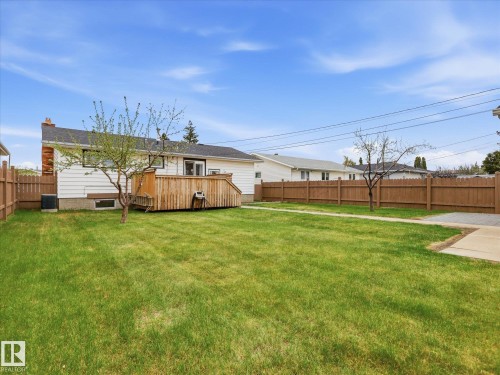 Expansive grassy yard with full perimeter fencing, a concrete patio area, and a wooden deck - 13504 116 St Nw, Edmonton, AB - Outdoor