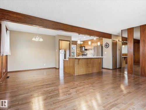 Open-concept living space with light wood-finish flooring, a wood beam accent, and a breakfast bar - 13504 116 St Nw, Edmonton, AB - Indoor Photo Showing Kitchen
