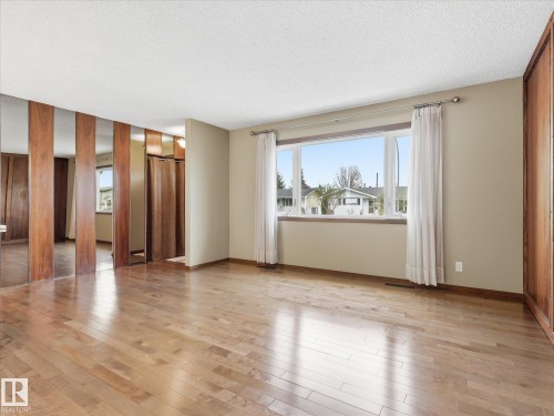 Bright living area featuring wood-finish flooring, a large picture window with a sill, and a mirrored accent wall with vertical wood panels - 13504 116 St Nw, Edmonton, AB - Indoor