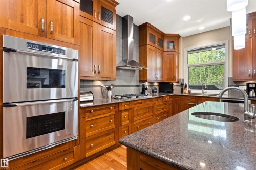 Kitchen featuring rich wood cabinetry, stainless steel double wall ovens, a coordinating stainless range hood, and speckled countertops - 1728 Rutherford Pt Point(E) Sw, Edmonton, AB - Indoor Photo Showing Kitchen
