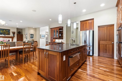 Spacious kitchen featuring a large central island with a dark countertop and undermount sink, stainless steel appliances, rich wood cabinetry, and wood-finish flooring - 1728 Rutherford Pt Point(E) Sw, Edmonton, AB - Indoor