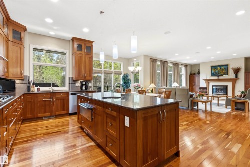 Spacious kitchen featuring an expansive center island with pendant lighting, wood-finish flooring, ample cabinetry, and an open concept layout - 1728 Rutherford Pt Point(E) Sw, Edmonton, AB - Indoor Photo Showing Kitchen With Fireplace