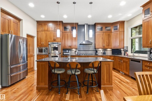 Kitchen featuring rich wood cabinetry, stainless steel appliances, a center island with countertop seating, recessed lighting, and wood-finish flooring - 1728 Rutherford Pt Point(E) Sw, Edmonton, AB - Indoor Photo Showing Kitchen With Upgraded Kitchen