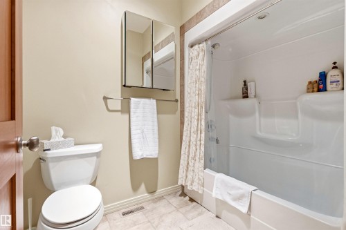 Full bathroom featuring a white tub/shower combination, light-toned wall tile surround, neutral painted walls, and a mirrored medicine cabinet - 1728 Rutherford Pt Point(E) Sw, Edmonton, AB - Indoor Photo Showing Bathroom
