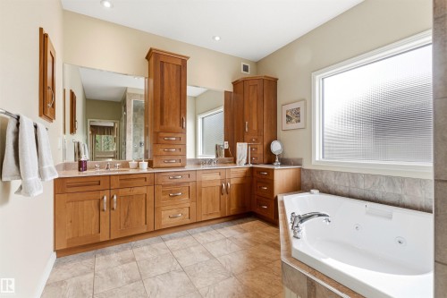 Spacious bathroom featuring a dual vanity with light wood cabinetry, a built-in jetted tub, a large privacy window, and tiled flooring - 1728 Rutherford Pt Point(E) Sw, Edmonton, AB - Indoor Photo Showing Bathroom