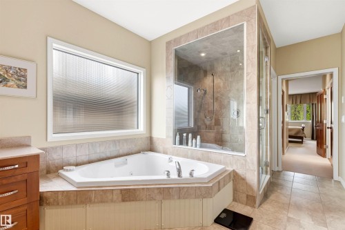 Bathroom featuring a corner soaking tub with tile surround, a glass-enclosed shower with tile walls, a window with textured glass, and wood-finish cabinetry with a countertop - 1728 Rutherford Pt Point(E) Sw, Edmonton, AB - Indoor Photo Showing Bathroom