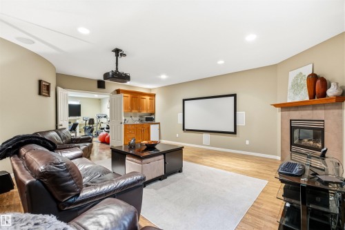 Entertainment room featuring a projection screen, built-in projector, recessed lighting, wood-finish flooring, and a fireplace with a tile surround and wood mantel - 1728 Rutherford Pt Point(E) Sw, Edmonton, AB - Indoor Photo Showing Living Room With Fireplace