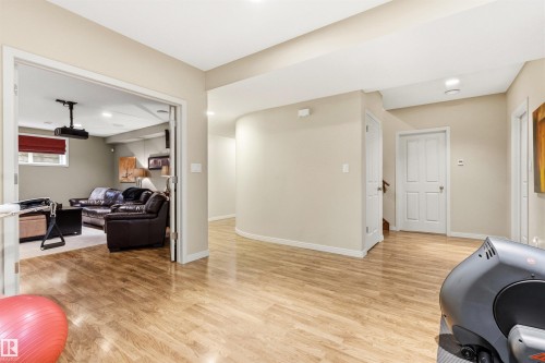 Bright lower level showcasing wood-finish flooring, recessed lighting, a curved wall detail, and a paneled door leading to an interior space - 1728 Rutherford Pt Point(E) Sw, Edmonton, AB - Indoor
