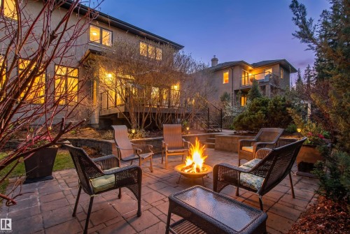 Expansive paver patio with a central fire pit, surrounded by tiered landscaping and illuminated by exterior lighting - 1728 Rutherford Pt Point(E) Sw, Edmonton, AB - Outdoor With Deck Patio Veranda