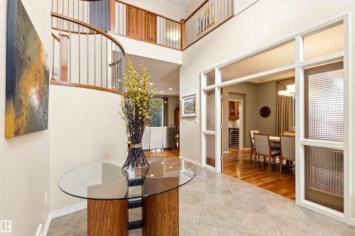 Two-story foyer featuring a curved staircase with wood and metal railing, textured tile flooring, and a double-height ceiling - 1728 Rutherford Pt Point(E) Sw, Edmonton, AB - Indoor Photo Showing Other Room