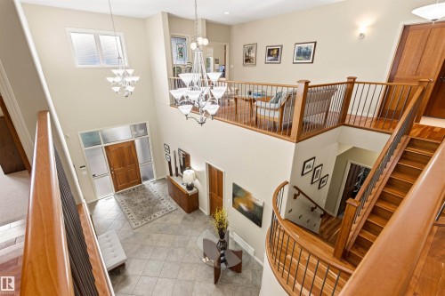 Two-story entryway featuring a wood front door with sidelight windows, tile flooring, and a grand staircase with wood banisters and metal spindles - 1728 Rutherford Pt Point(E) Sw, Edmonton, AB - Indoor Photo Showing Other Room