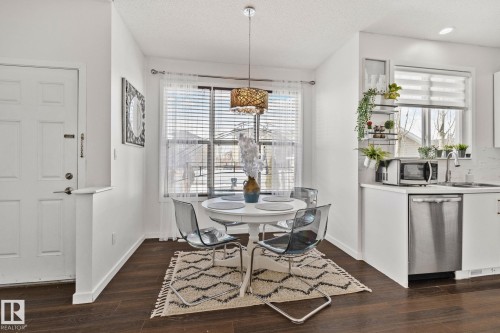 The property offers an open-concept dining area with dark wood flooring, a modern chandelier, and a large window providing natural light - 336 Southfork Drive, Leduc, AB - Indoor Photo Showing Dining Room