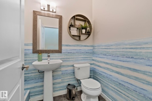 The bathroom features a pedestal sink with a modern faucet, a mirror with a decorative frame, and unique blue-toned striped wall covering - 336 Southfork Drive, Leduc, AB - Indoor Photo Showing Bathroom