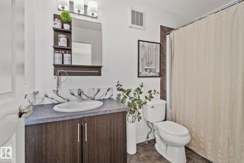 The bathroom features a vanity with a dark wood cabinet, a white oval sink, and a marble-patterned backsplash - 336 Southfork Drive, Leduc, AB - Indoor Photo Showing Bathroom