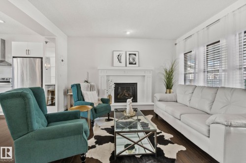 This inviting living area features dark wood flooring, a white fireplace with a mantel, and bright windows - 336 Southfork Drive, Leduc, AB - Indoor Photo Showing Living Room With Fireplace