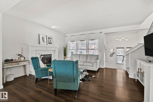 The living room features rich wood flooring, a white fireplace with an ornate mantel, and large windows with blinds and sheer curtains - 336 Southfork Drive, Leduc, AB - Indoor Photo Showing Living Room