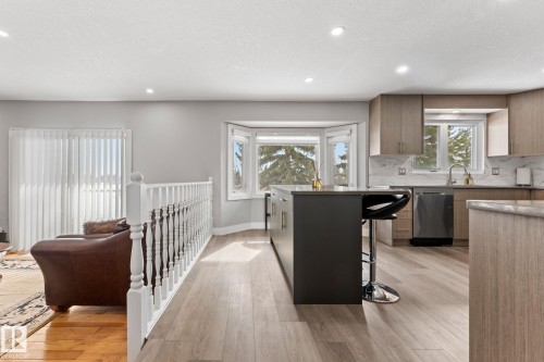 Contemporary kitchen featuring light wood cabinetry, a dark kitchen island with seating, a stainless steel dishwasher, and a bay window providing natural light - 10673 161 Avenue, Edmonton, AB - Indoor Photo Showing Kitchen With Double Sink