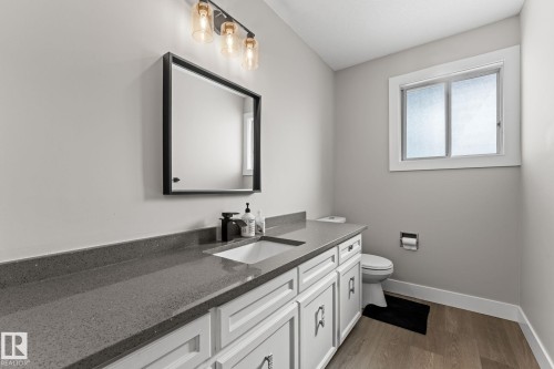 The bathroom features a vanity with a gray countertop and white cabinetry, a rectangular mirror with a black frame, and a window providing natural light - 10673 161 Avenue, Edmonton, AB - Indoor Photo Showing Bathroom