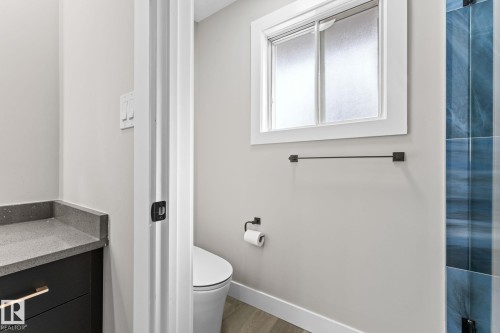The bathroom features a window for natural light, a modern toilet, and a vanity with a grey countertop and dark cabinetry - 10673 161 Avenue, Edmonton, AB - Indoor Photo Showing Bathroom