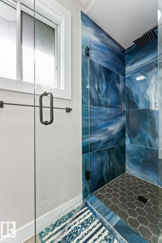 Modern shower featuring striking blue wall tiles, a black hexagonal floor, and a black rainfall showerhead - 10673 161 Avenue, Edmonton, AB - Indoor Photo Showing Other Room