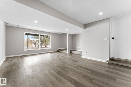 Spacious room featuring light wood-style flooring, light-colored walls, recessed lighting, and a large window providing views of trees - 10673 161 Avenue, Edmonton, AB - Indoor