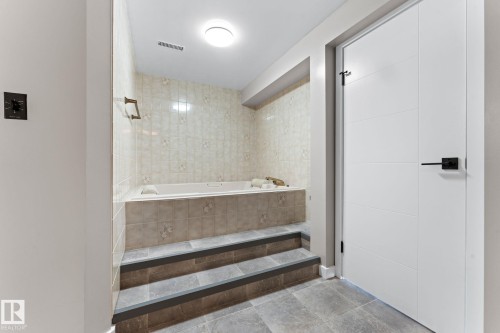 Bathroom featuring a built-in tub with surrounding tile, steps leading to the tub, and a white modern door with a black handle - 10673 161 Avenue, Edmonton, AB - Indoor