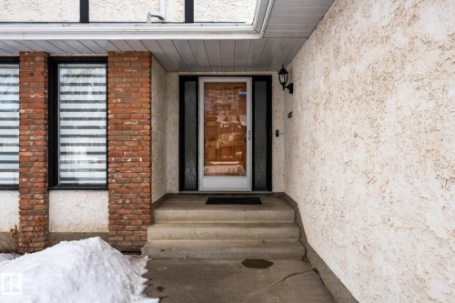 The property features a front entrance with concrete steps and a textured stucco exterior, complemented by brick detailing around the windows - 10673 161 Avenue, Edmonton, AB - Outdoor