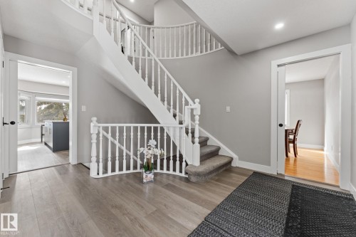 The property features a grand curved staircase with white balusters and carpeted treads, complemented by light grey walls and wide plank flooring - 10673 161 Avenue, Edmonton, AB - Indoor Photo Showing Other Room