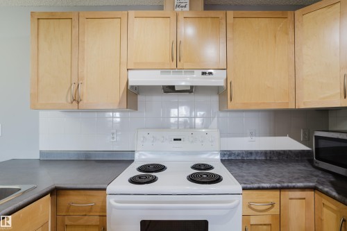 Kitchen featuring light wood cabinetry, a white electric range, white subway tile backsplash, and dark laminate countertops - 508 11103 84 Avenue, Edmonton, AB - Indoor Photo Showing Kitchen