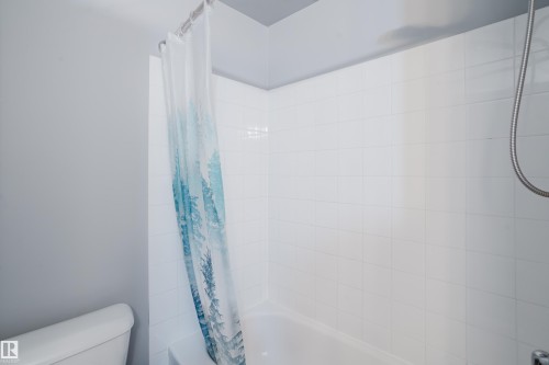 Bathtub and shower combination featuring white subway tile surround, chrome shower rod, and a handheld shower head - 508 11103 84 Avenue, Edmonton, AB - Indoor Photo Showing Bathroom
