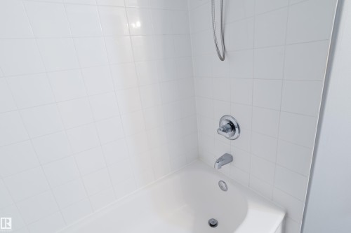 Bathtub and shower combination featuring white square wall tiles and chrome fixtures - 508 11103 84 Avenue, Edmonton, AB - Indoor Photo Showing Bathroom