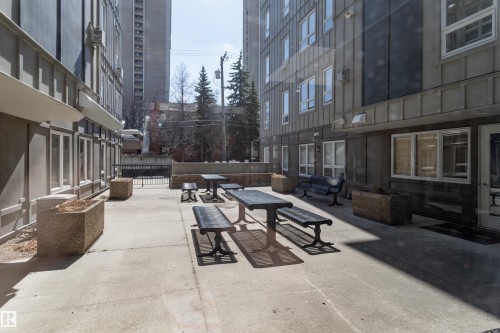 Concrete patio area with multiple picnic tables and benches, framed by concrete planters and building facades featuring white-framed windows - 508 11103 84 Avenue, Edmonton, AB - Outdoor With Exterior