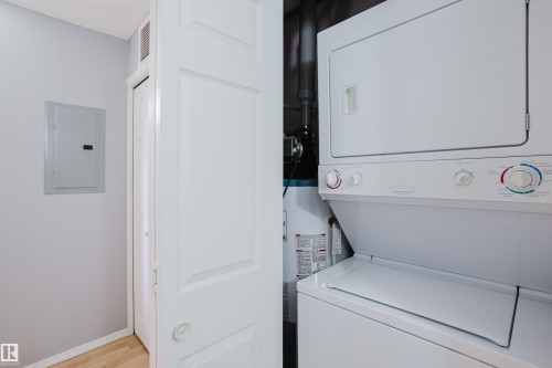 Dedicated laundry closet featuring a white stacked washer and dryer unit, a water heater, and light wood-finish flooring - 508 11103 84 Avenue, Edmonton, AB - Indoor Photo Showing Laundry Room