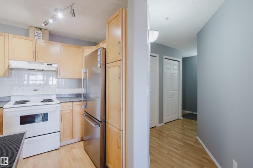 Kitchen featuring wood-finish cabinetry, white tile backsplash, and a stainless steel refrigerator - 508 11103 84 Avenue, Edmonton, AB - Indoor Photo Showing Kitchen