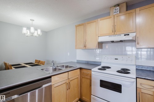 Kitchen featuring wood-finish cabinetry, a stainless steel double sink, and a stainless steel dishwasher - 508 11103 84 Avenue, Edmonton, AB - Indoor Photo Showing Kitchen With Double Sink
