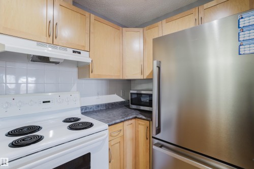 Kitchen featuring light wood-finish cabinetry, a white electric range with overhead ventilation, a white tile backsplash, and a stainless steel refrigerator - 508 11103 84 Avenue, Edmonton, AB - Indoor Photo Showing Kitchen